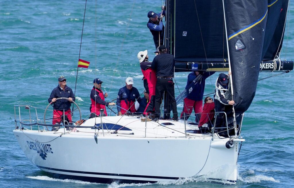 Close up photo of Checkmate sailing on a reach, crew are adjusting something on the mast.